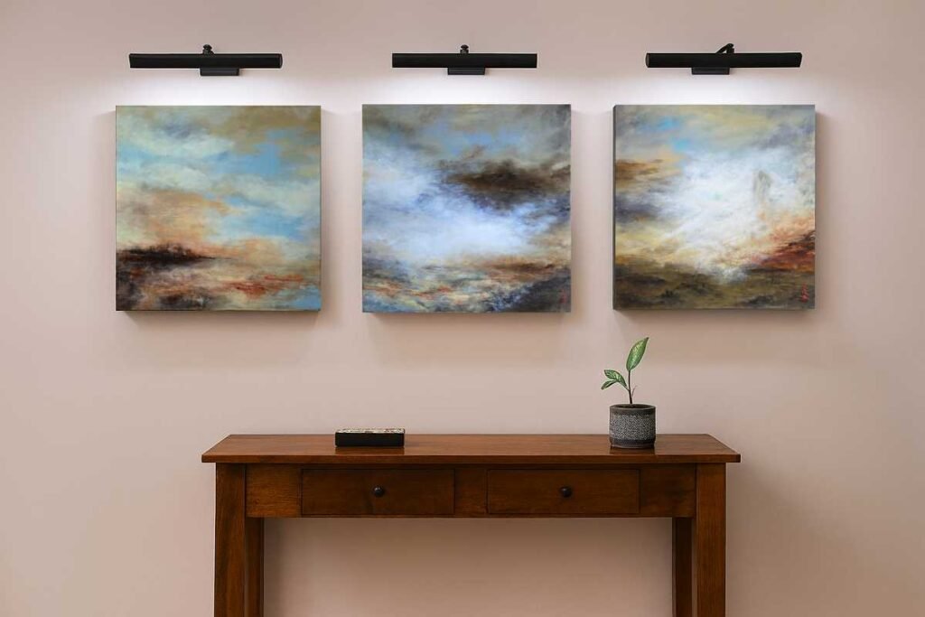 Three abstract landscape paintings mounted above a wooden console table with a small potted plant on the right.